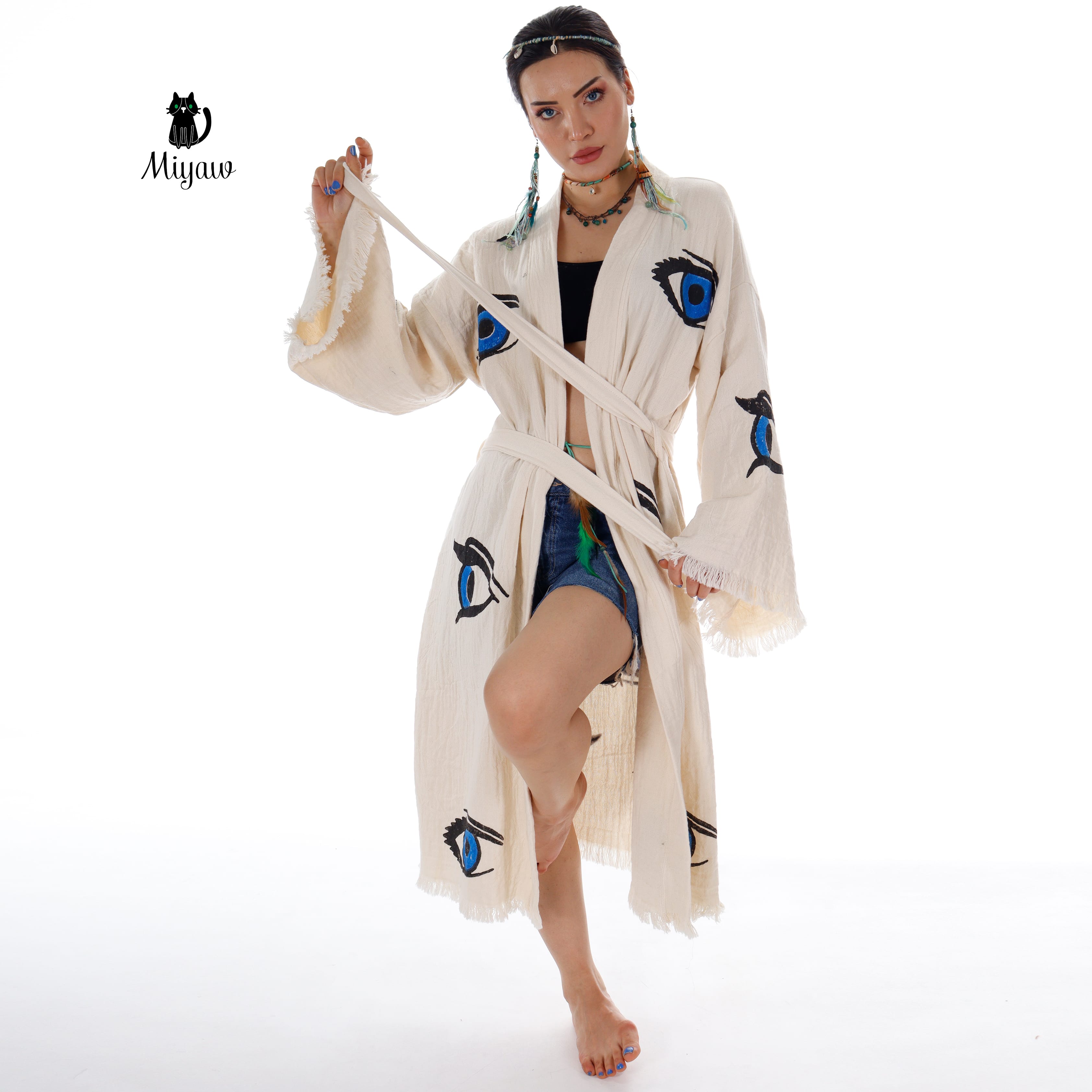 Model wearing MIYAW beige cotton beach kimono robe with blue eye motifs and adjustable tie